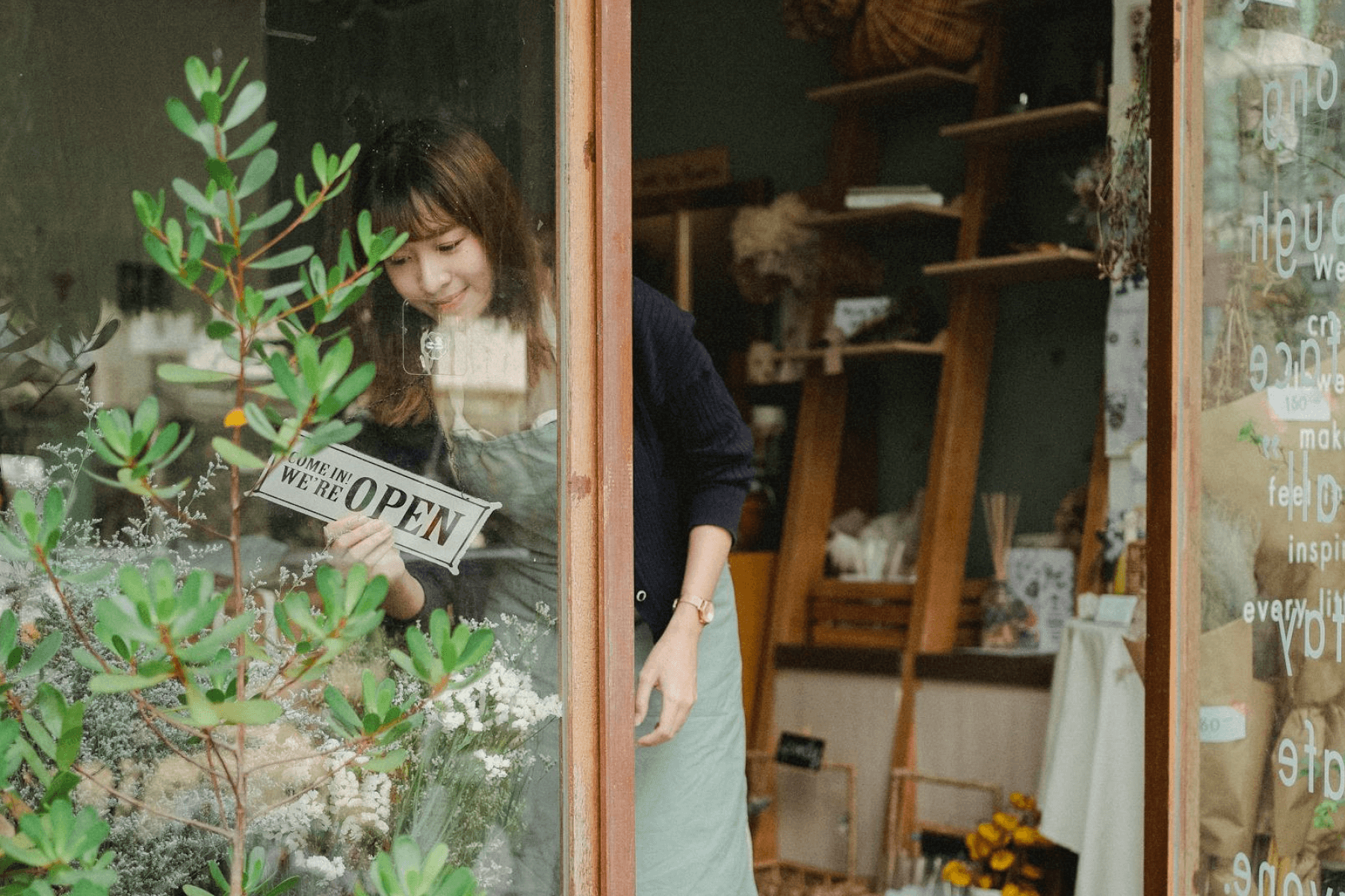 A woman stands in a store entryway hanging up a sign reading ‘Come in! We’re OPEN’ in a glass window.