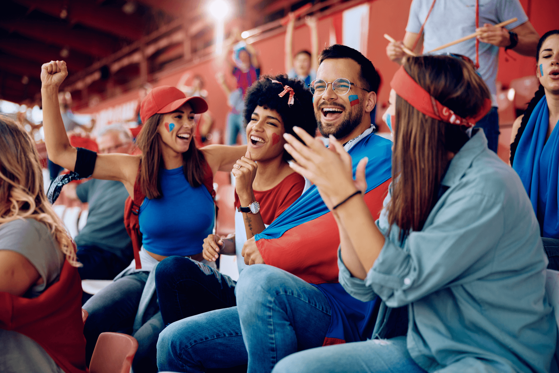 A group of men and women are cheering in the stands of a sports game while wearing red and blue team colors.