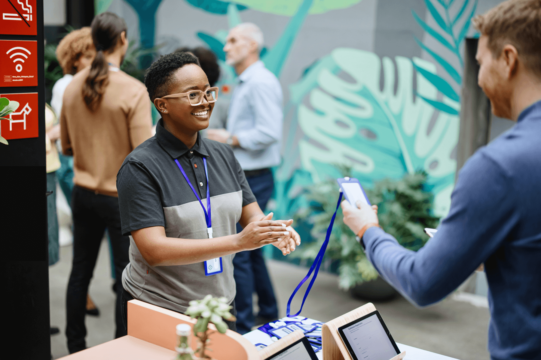 A person at a table hands a blue lanyard to someone while three other people chat in the background.