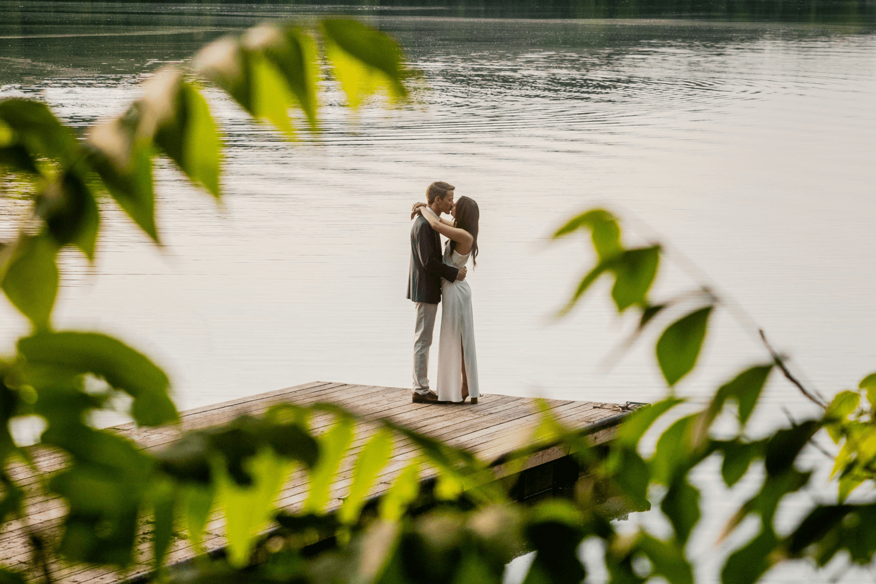 A couple is sharing a kiss while standing by a lake.