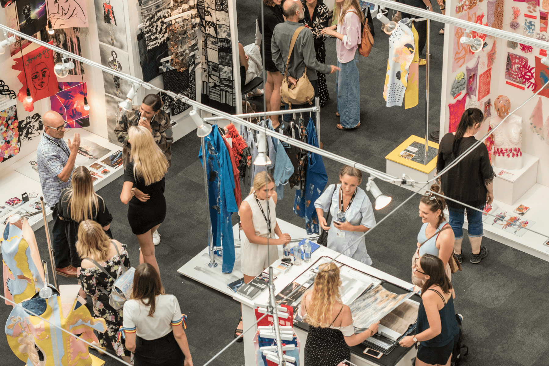 A crowd of people mingling at an event in a space with art and clothing displayed.