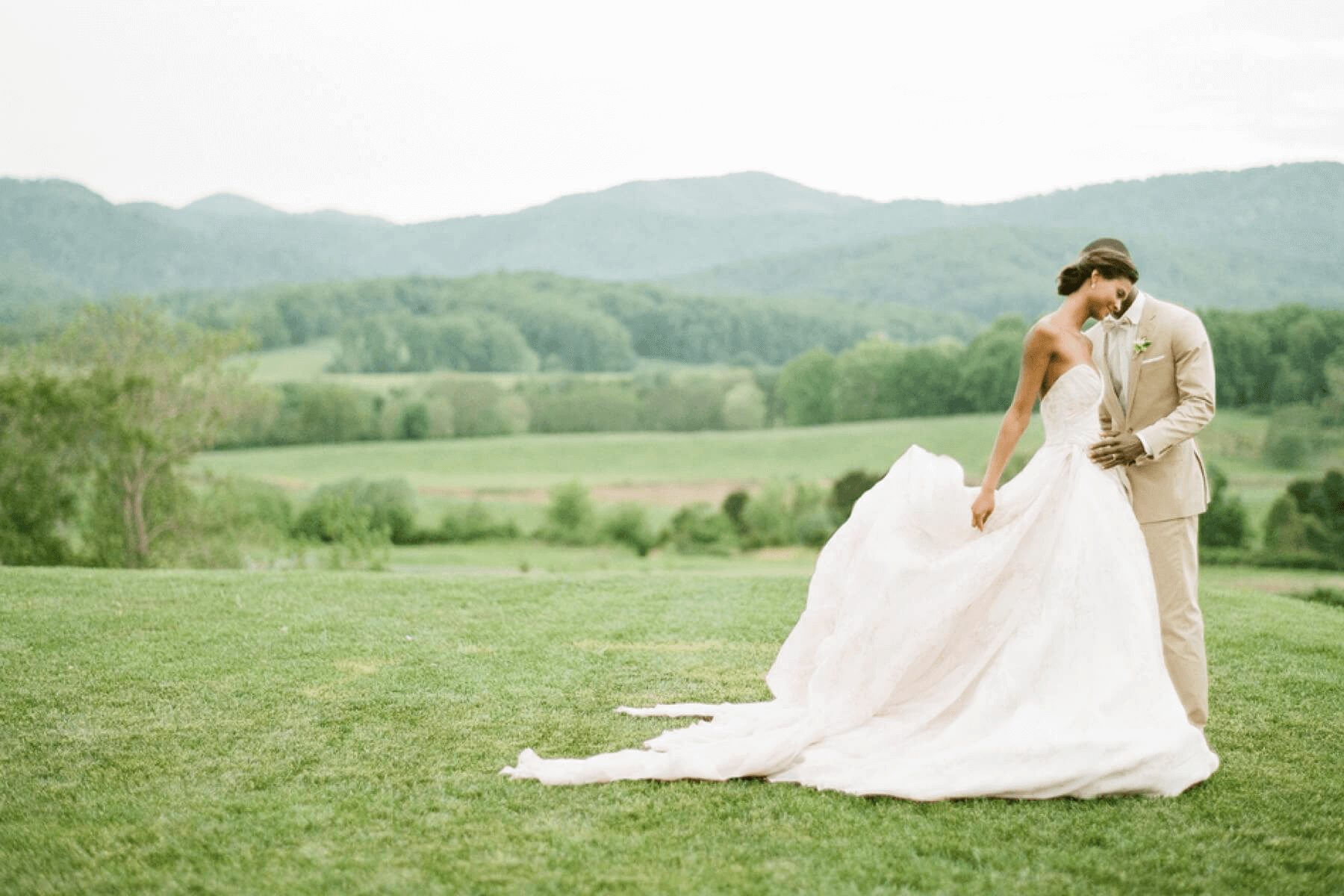 A bride and groom pose together in an expansive green field.