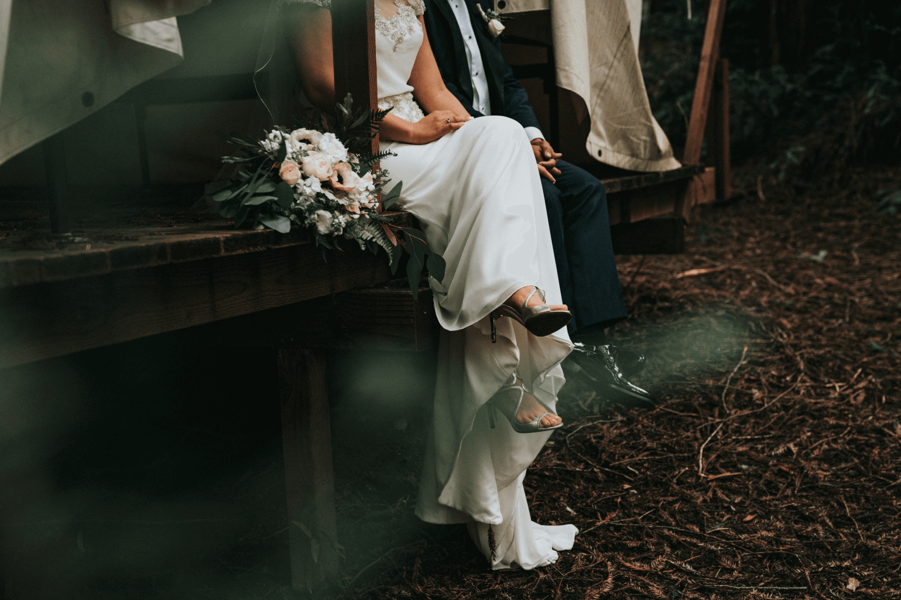 A bride and groom sit together with their legs hanging off a wooden porch.