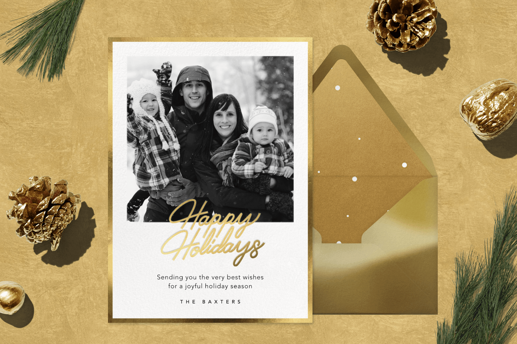 A holiday card featuring a black and white family photo over a gold background with holiday greenery and décor.