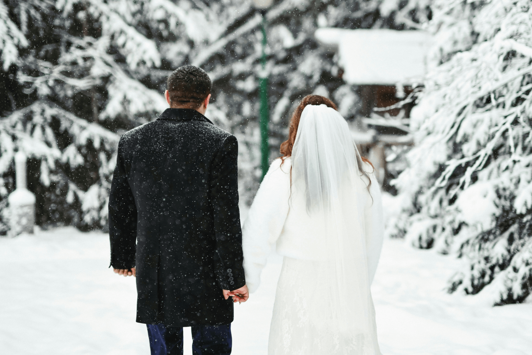 A bride and groom holding hands while walking together in the snow.