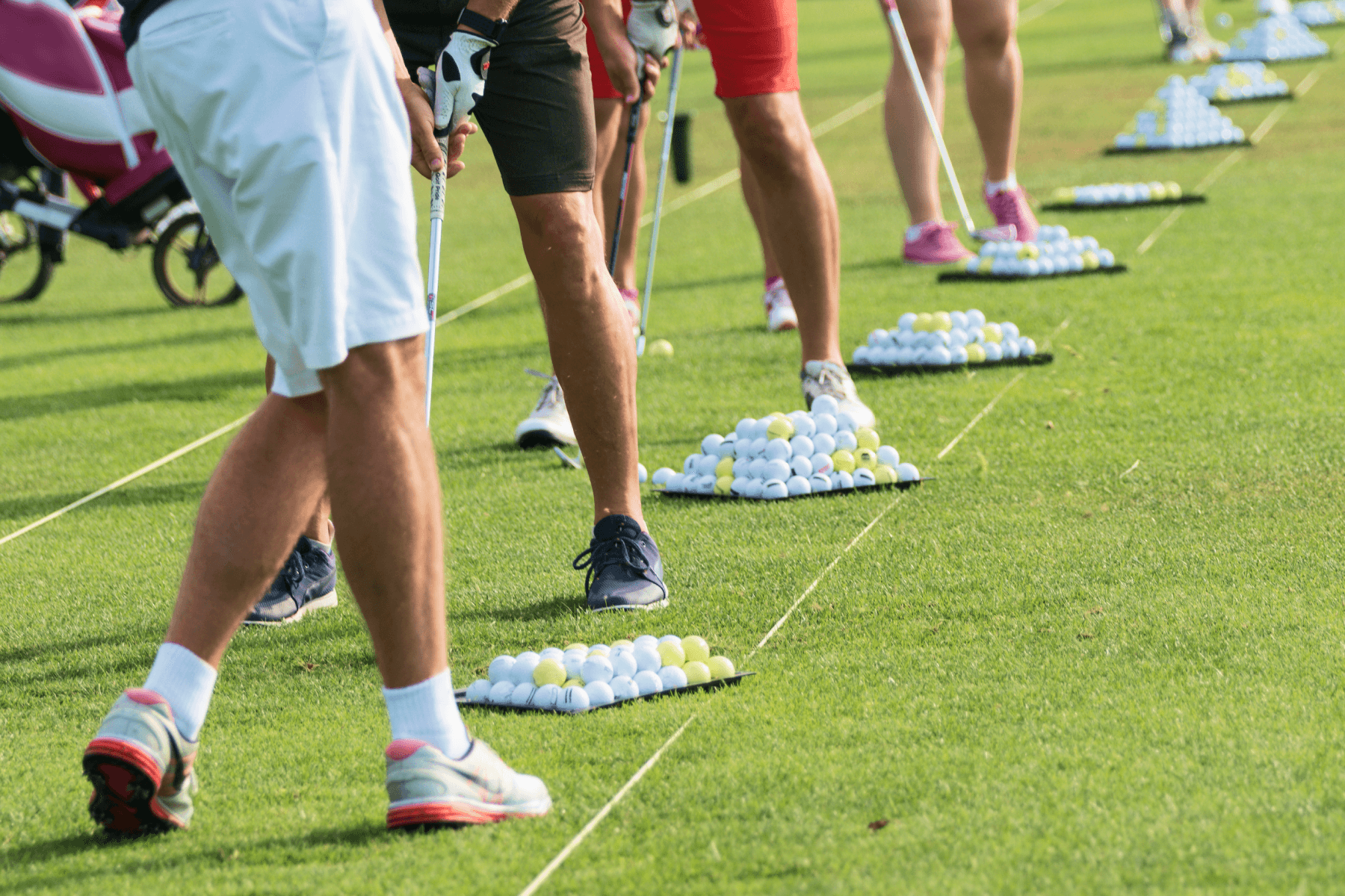 The legs of golfers lined up preparing to swing at nouns of golf balls.