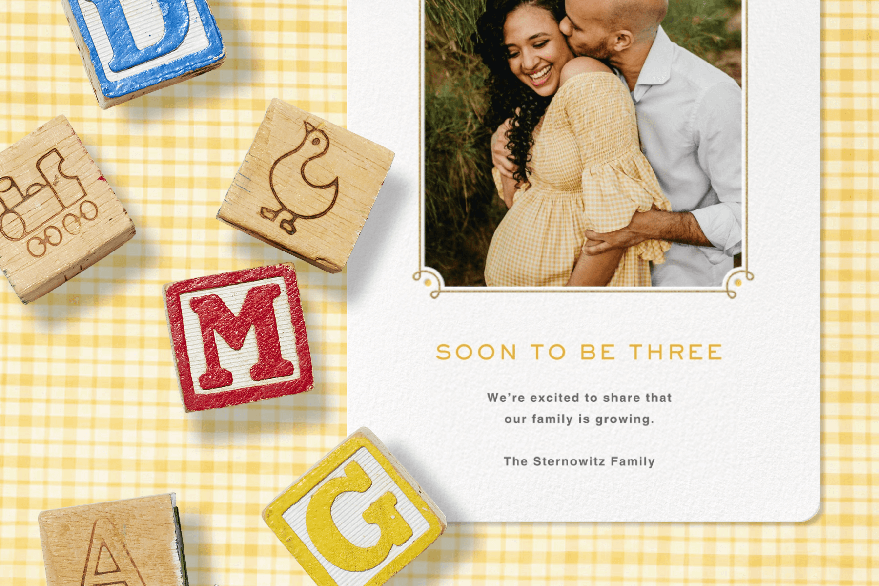 A pregnancy announcement card with a photo of the expecting couple over a yellow gingham backdrop with toy blocks.