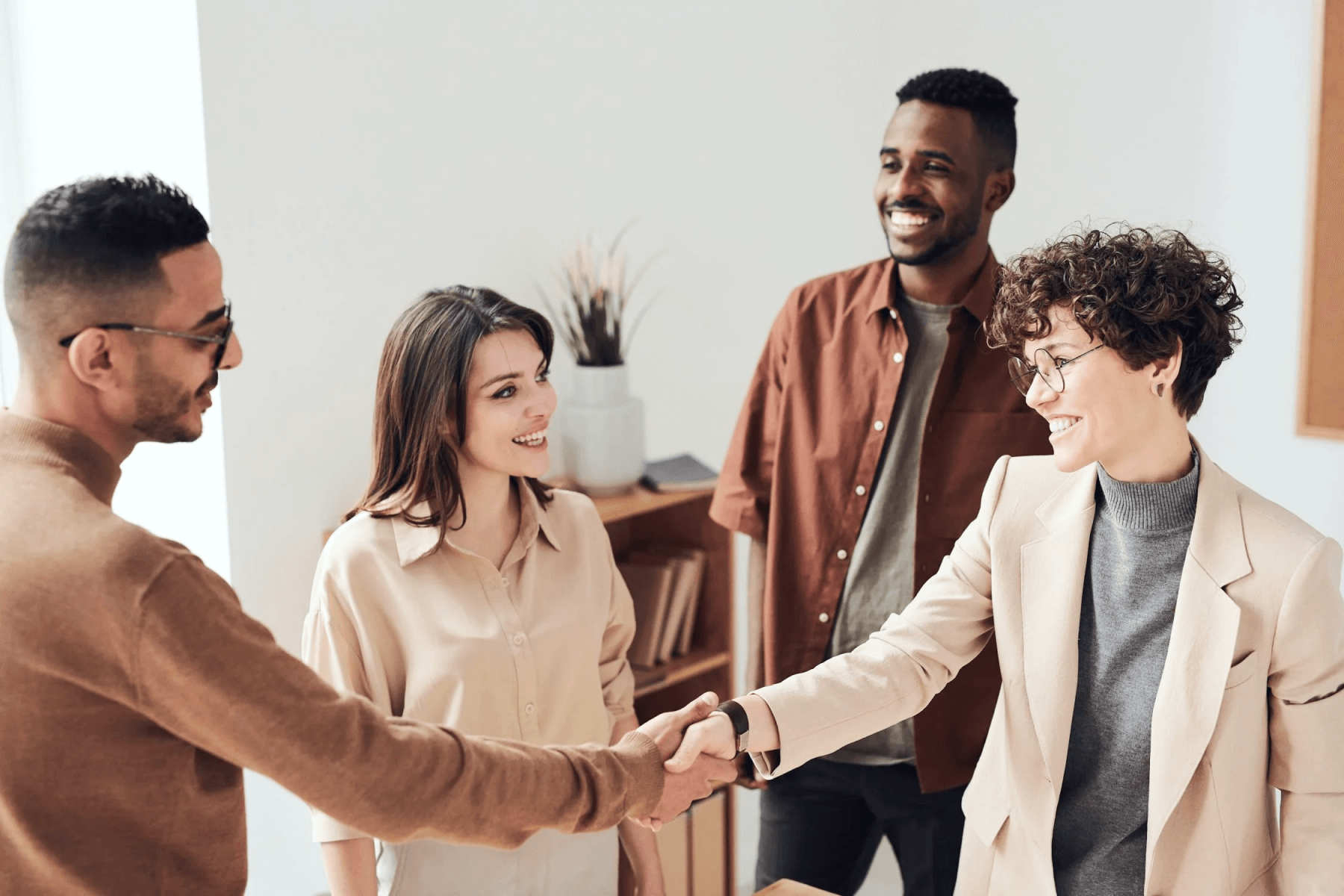 A group of people smiling together while two of them shake hands.