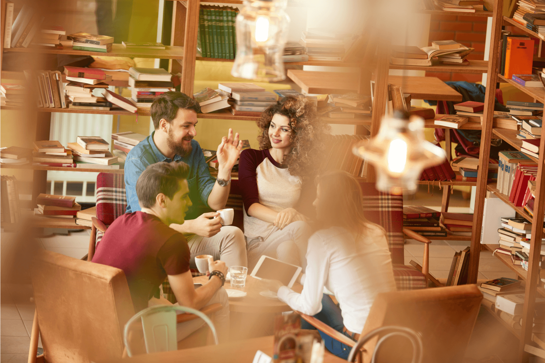 A group of four friends sitting at a table, talking and drinking coffee, surrounded by shelves of books.