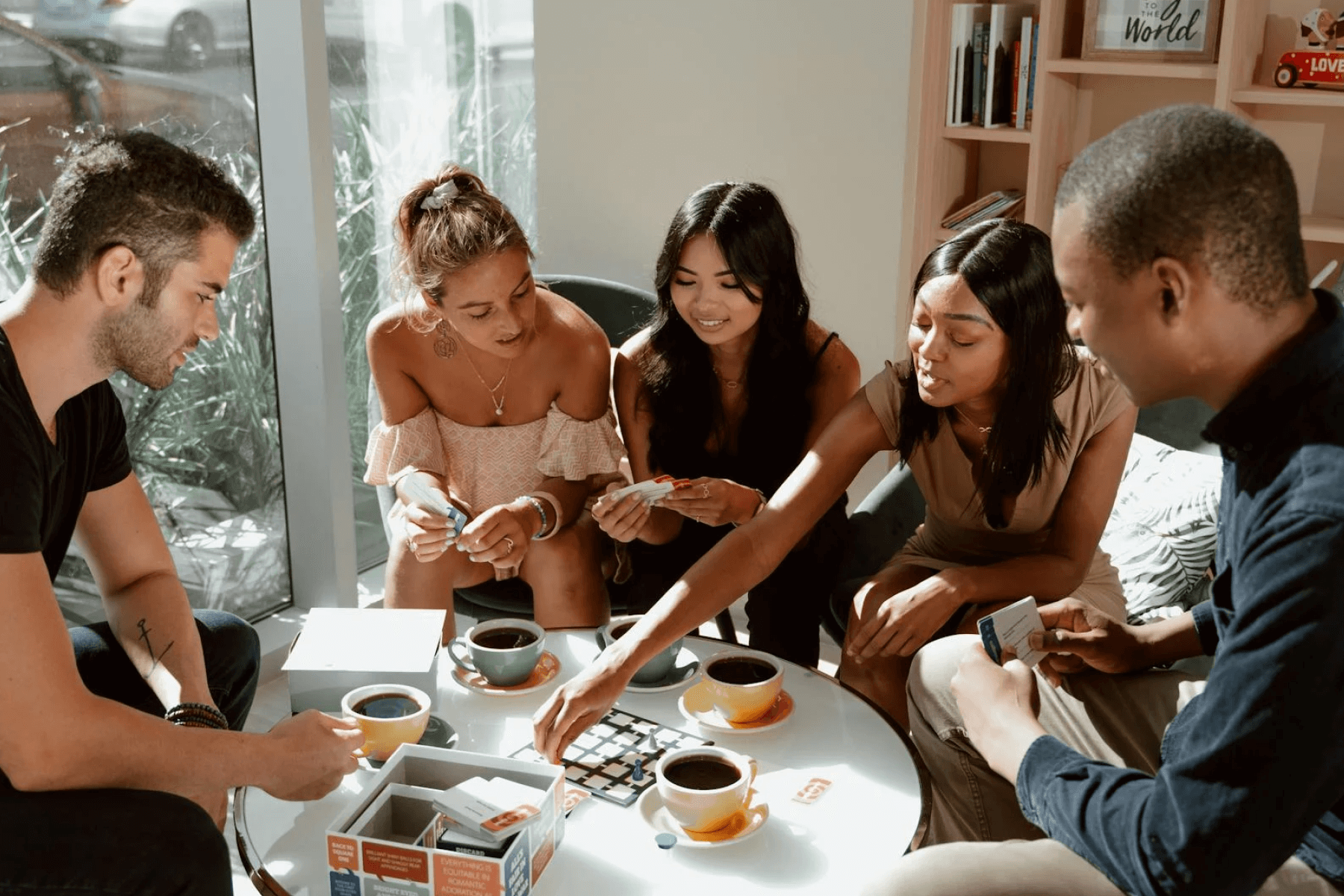 A group of friends sitting around a circular table with mugs of coffee while playing a board game.