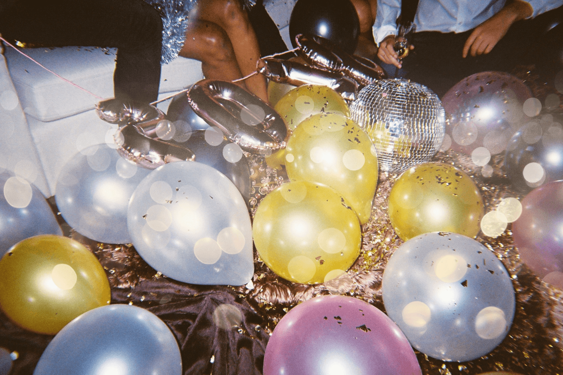 Yellow, white, and pink balloons, a disco ball, and confetti at a New Year’s Eve party.