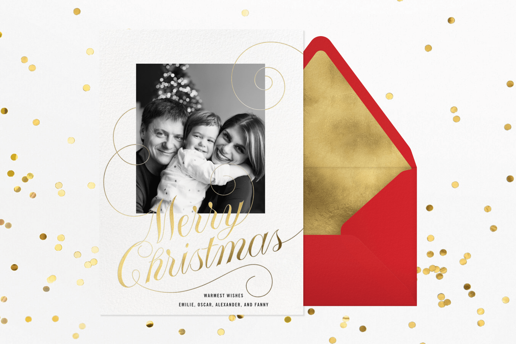 A Christmas card featuring a black and white photo of parents holding a child and gold cursive lettering reading ‘MERRY CHRISTMAS’. 