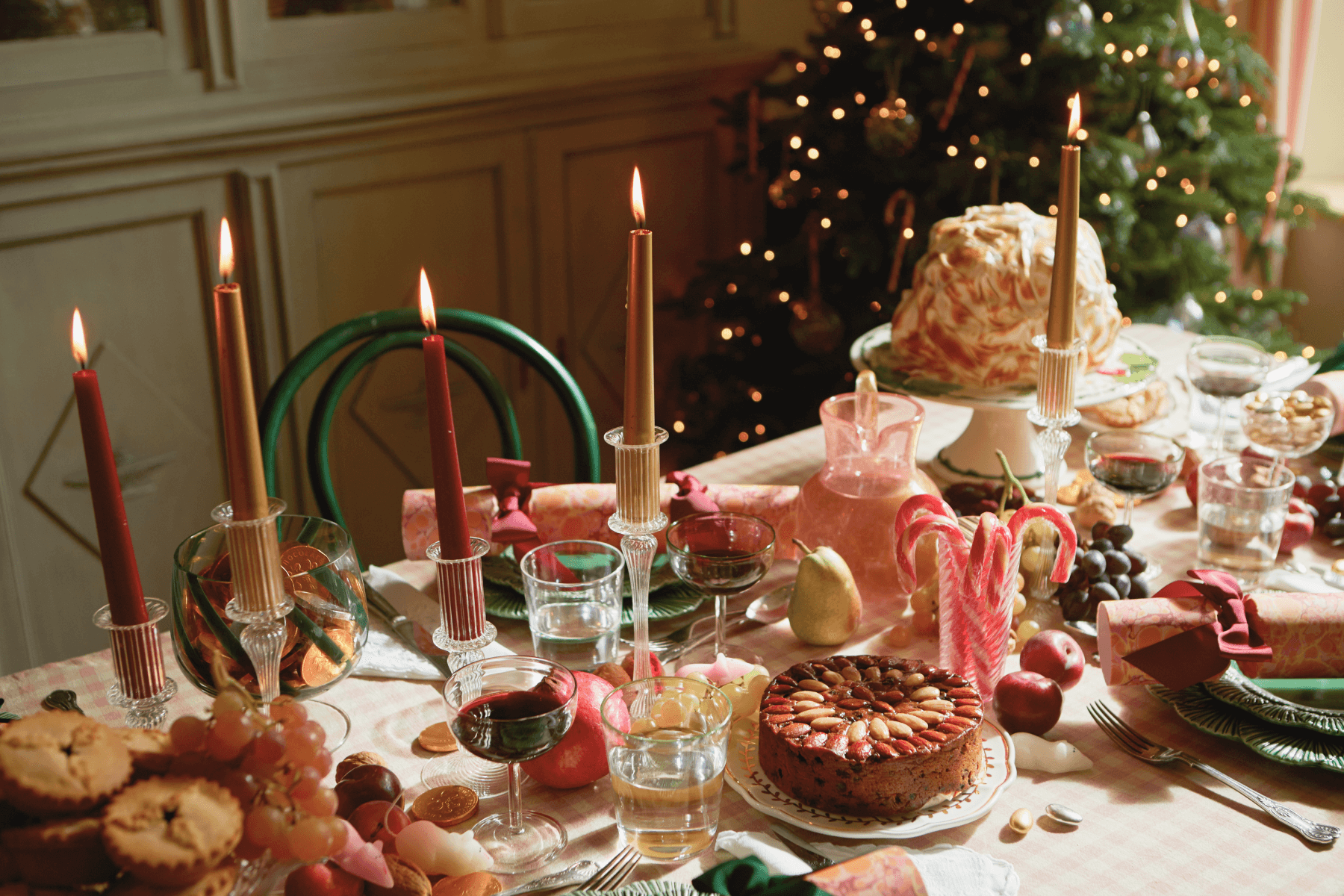 A dining table set with candles, drinks, candy canes, a cake, fruit, and crackers. 