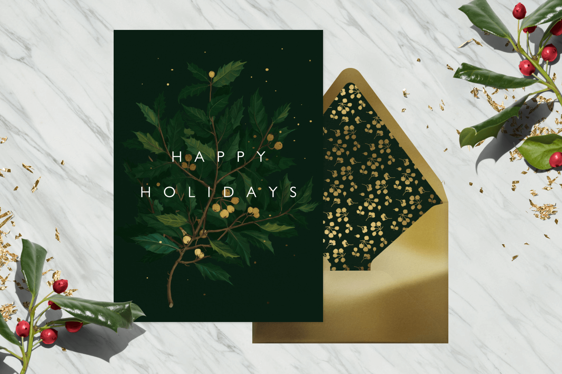 Green card with a holly branch reading Happy Holidays on top of a golden envelope and marble background