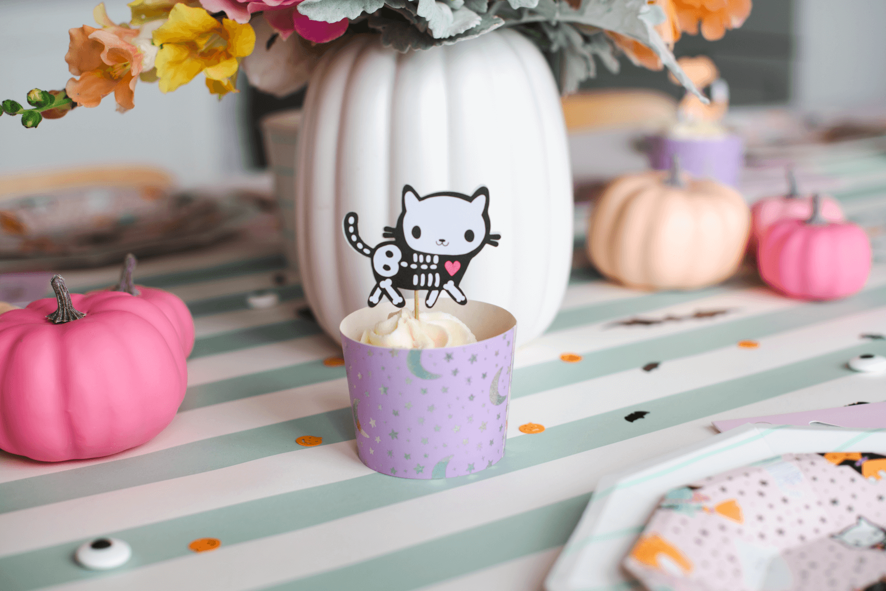 A purple cup with a cupcake and a skeleton cat on a toothpick. 