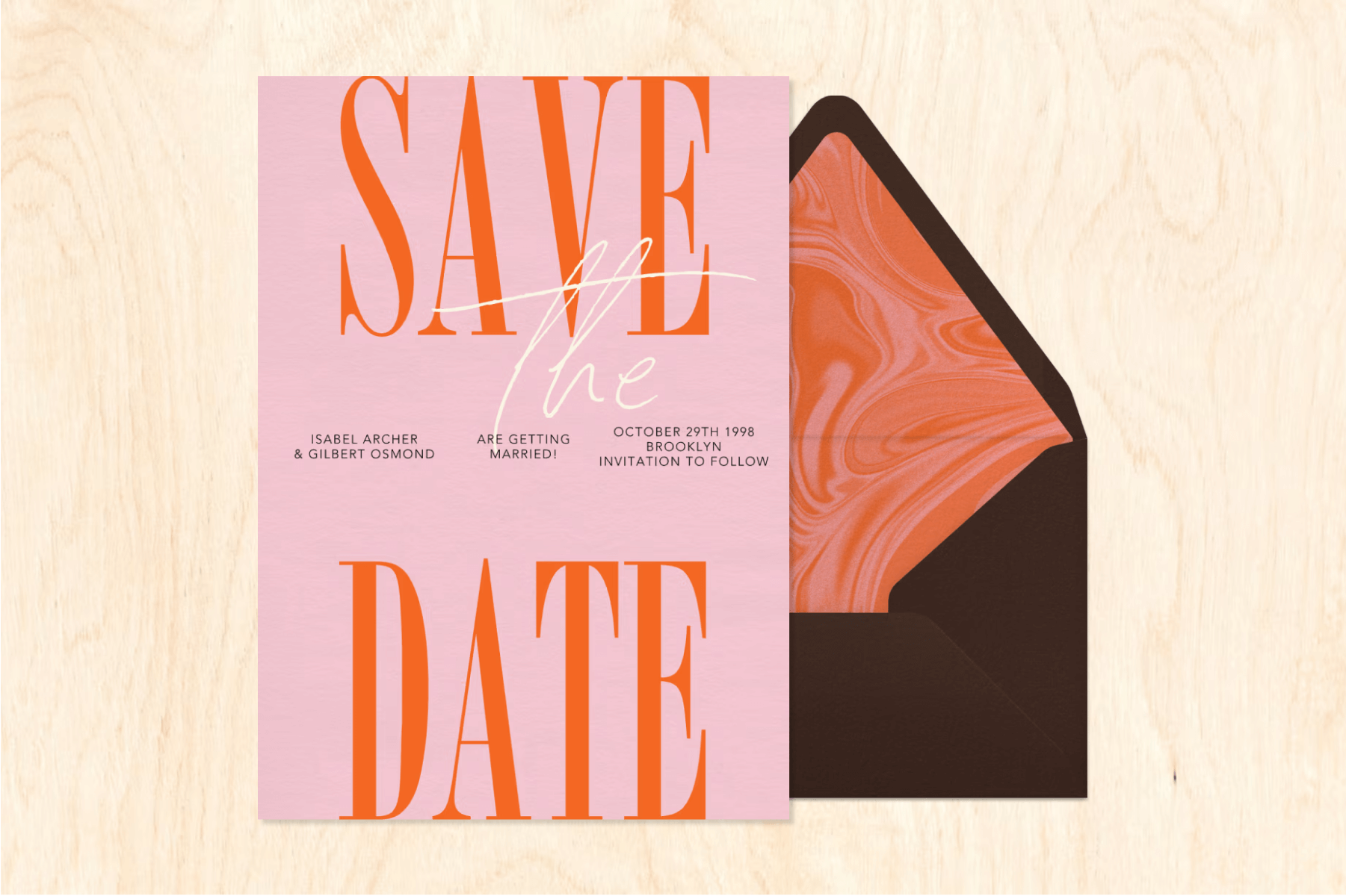 A pink card with large orange text reading ‘SAVE THE DATE’ over a light wood-grain-style backdrop.