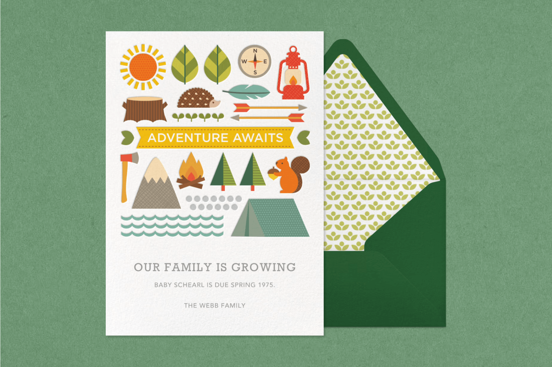 A pregnancy announcement card with camping-themed illustrations next to a green envelope and in front of a green backdrop.