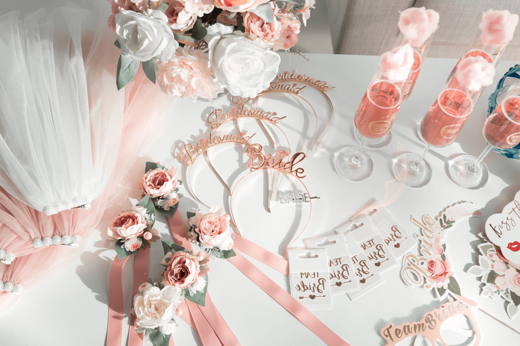 A table of bridal-themed party favors, flowers, and glasses of pink Champagne with cotton candy.