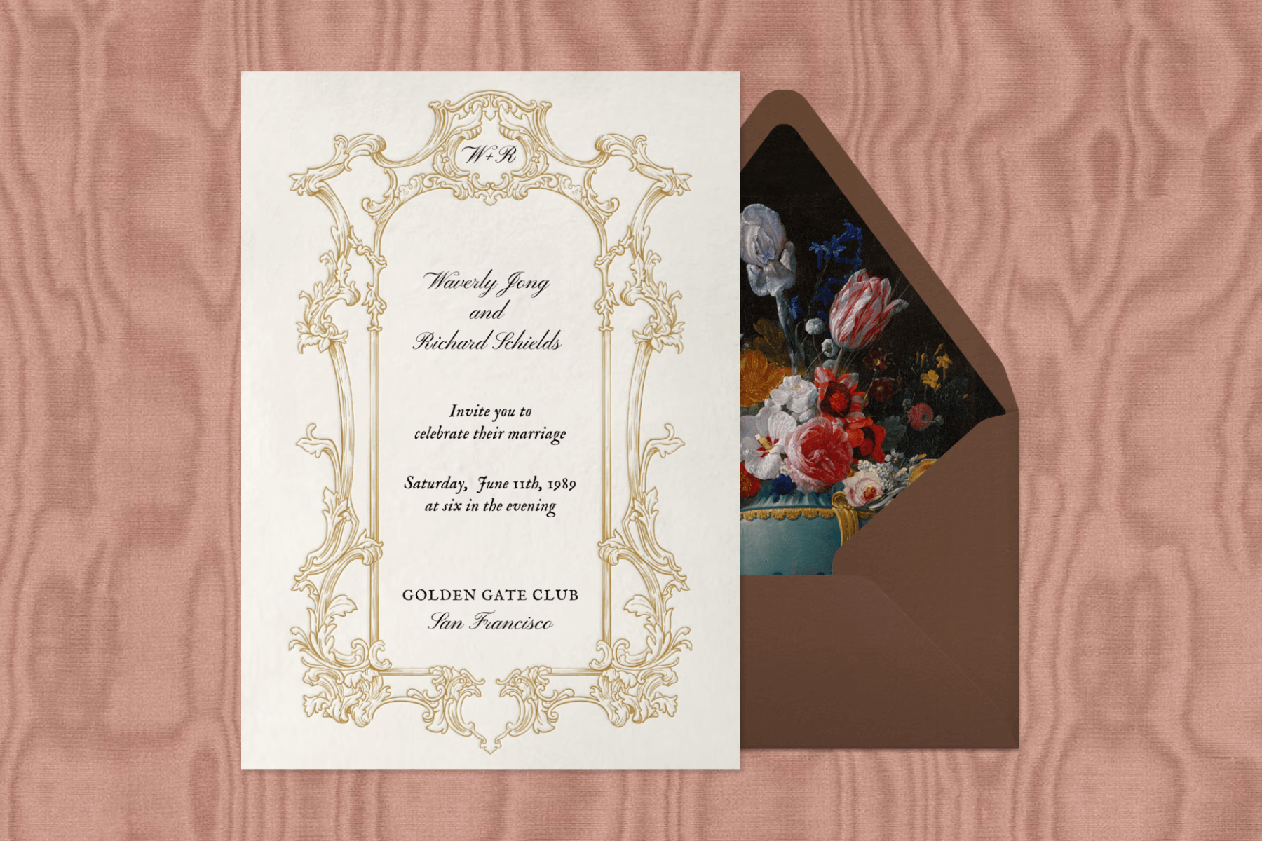 An off-white wedding invitation with a gold ornate frame and black cursive text. 