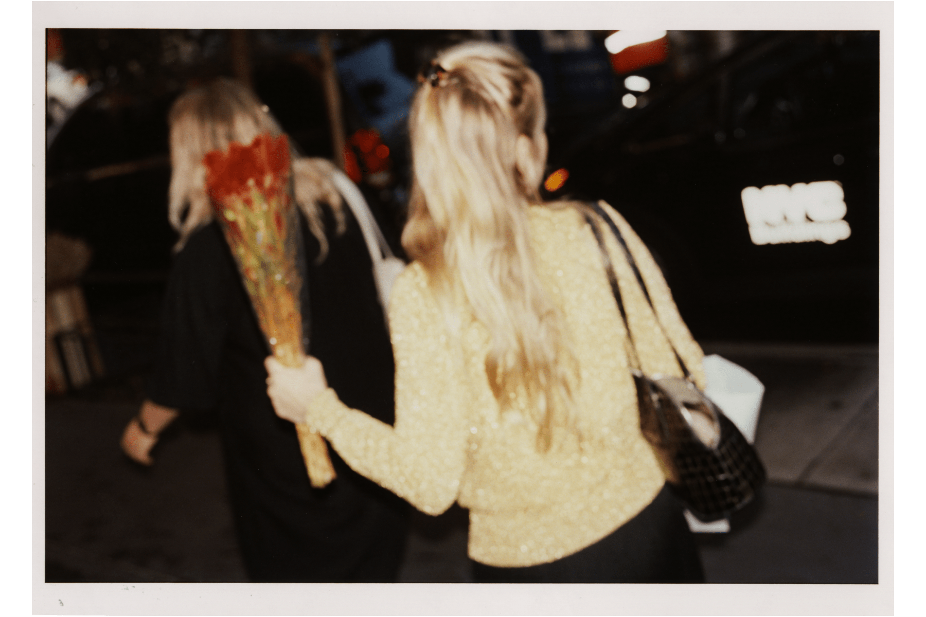 A blurred photo of Joana Avillez walking away from the camera holding a bouquet of red flowers.