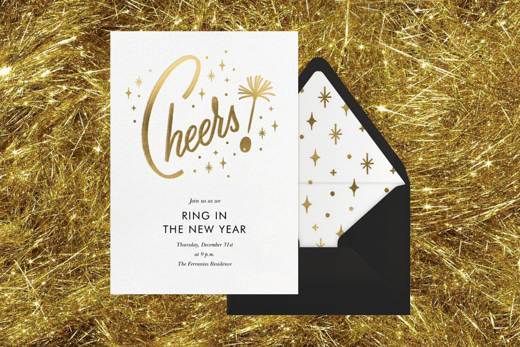 A white invitation with gold text reading ‘CHEERS!’ in front of a backdrop with gold tinsel. 