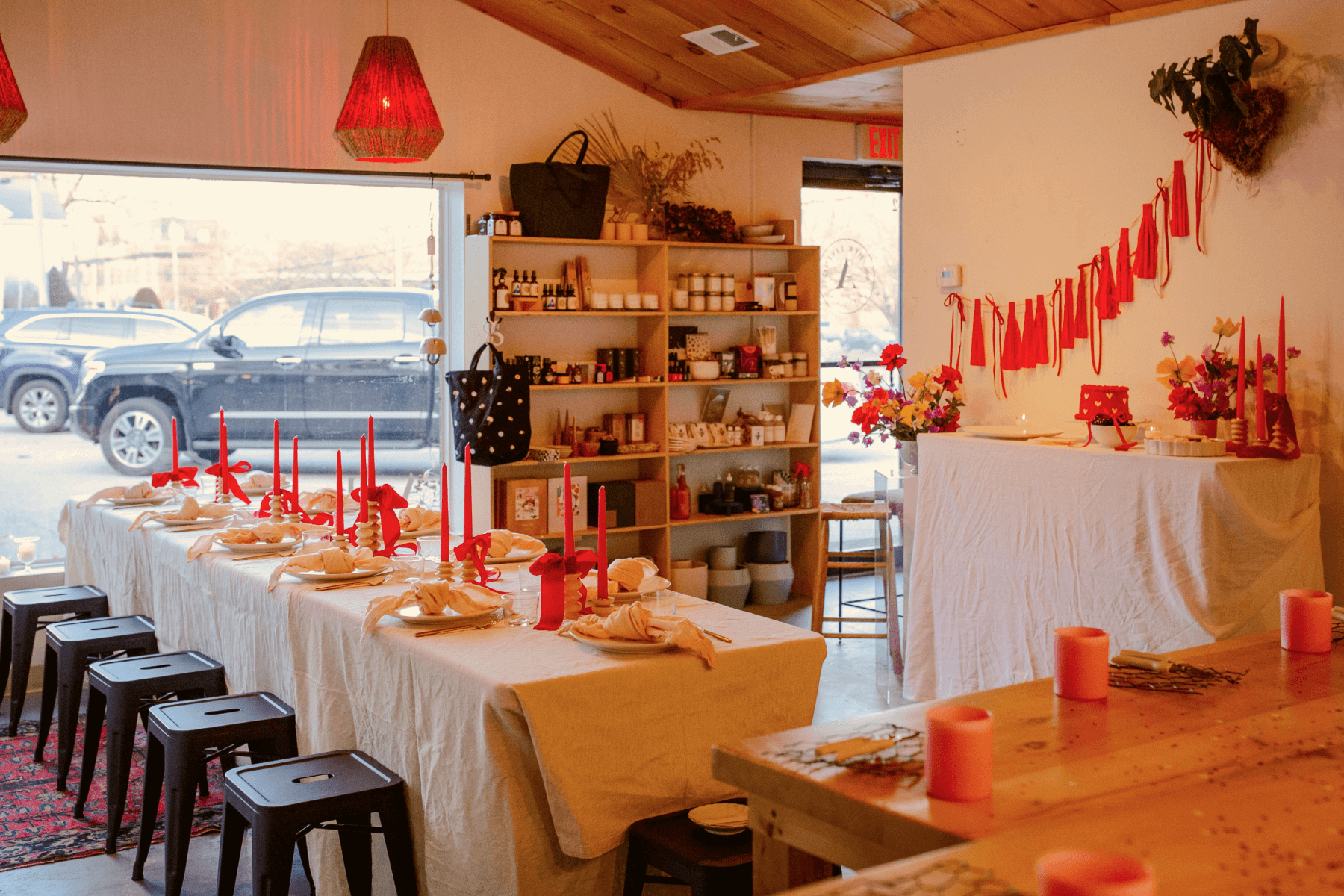 A store with shelves of goods and a table set for a Galentine’s Day event with a tablecloth, red candles, and plates with napkins. 