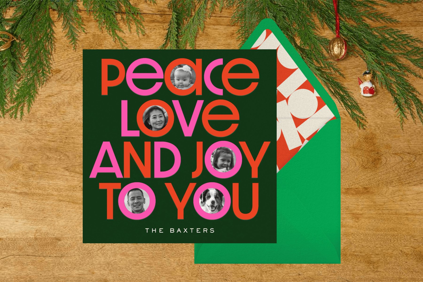 A holiday card with text reading ‘PEACE LOVE AND JOY TO YOU’ with family photos inside of the letters, over a wood background with greenery.