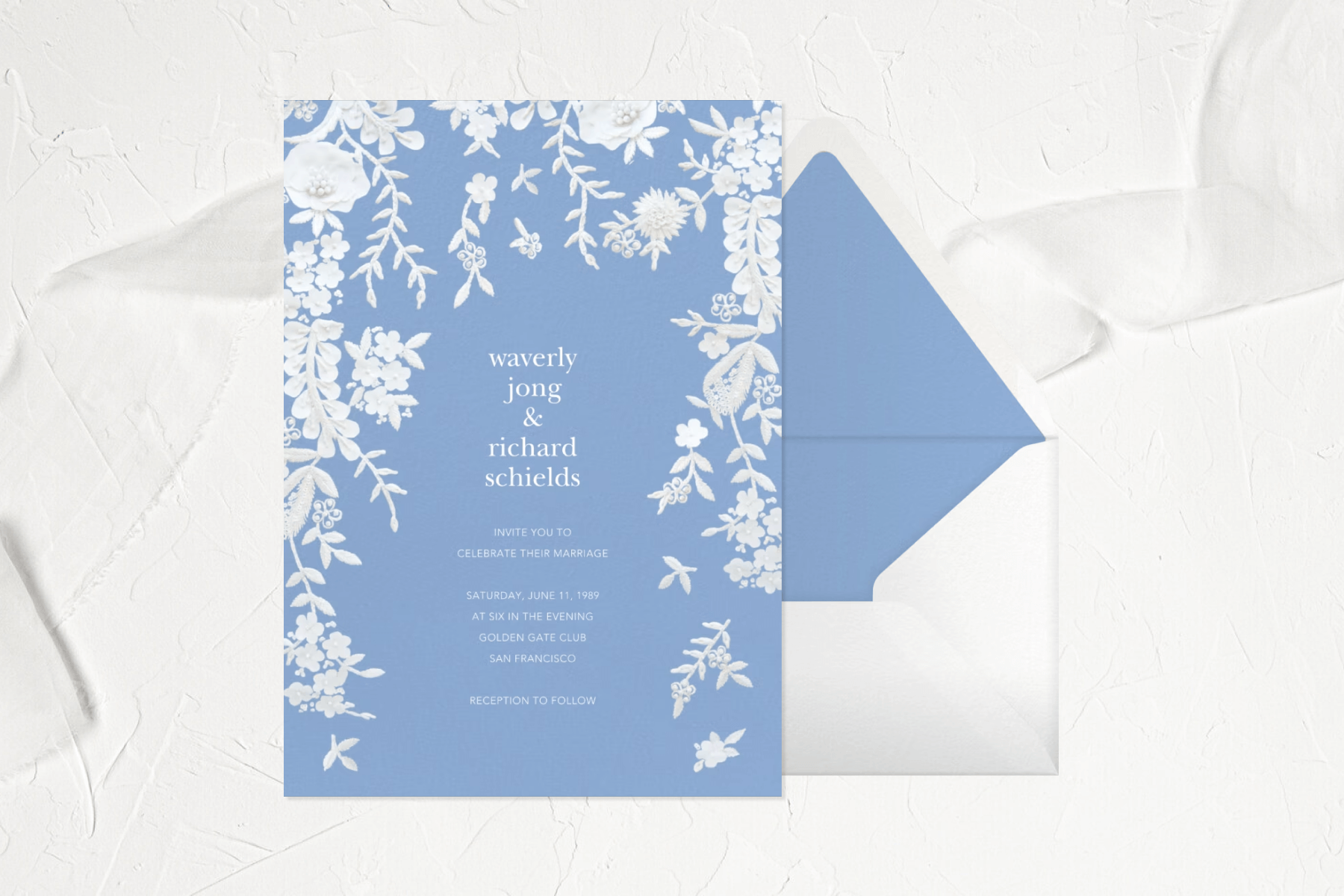 A light blue wedding invitation with white florals bordering the top and sides.  