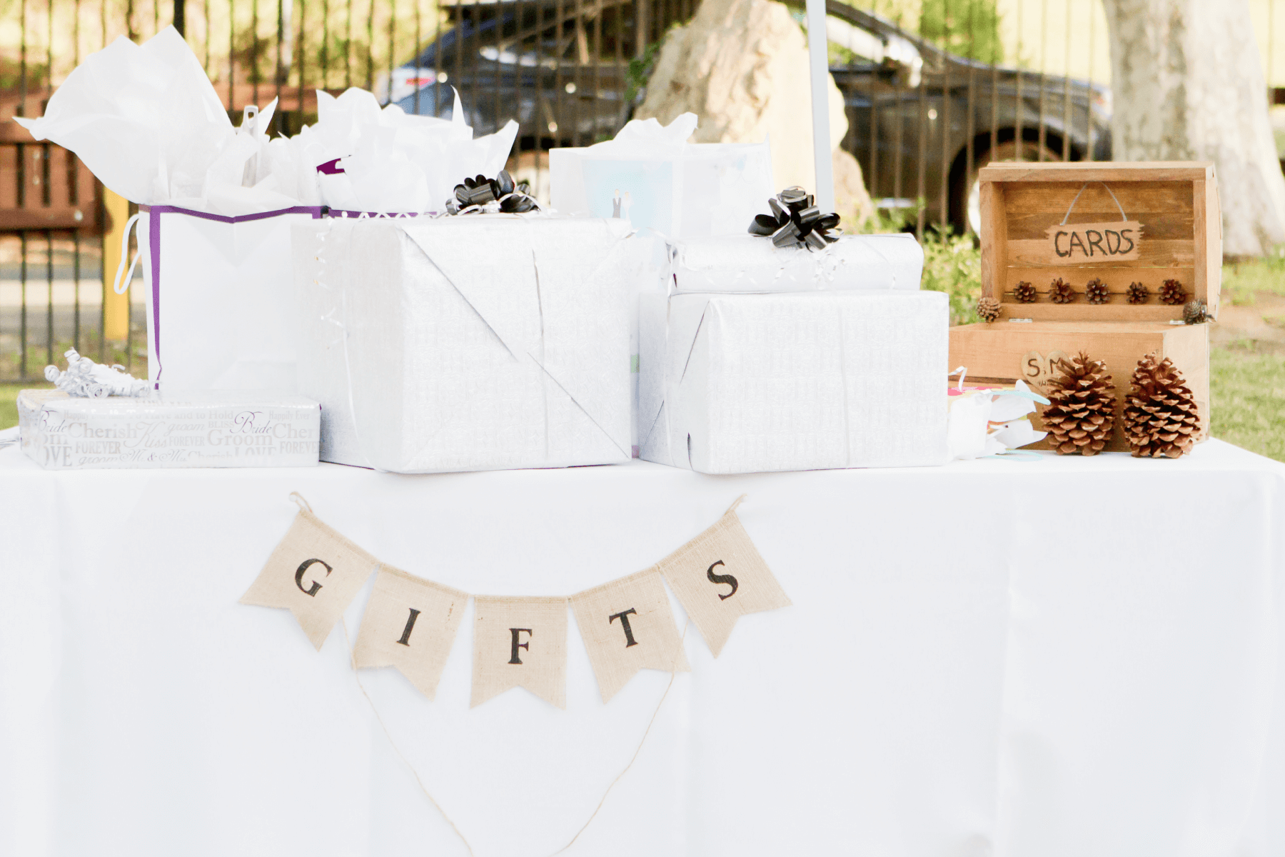 A gift table at an outdoor party topped with presents in white wrapping paper.